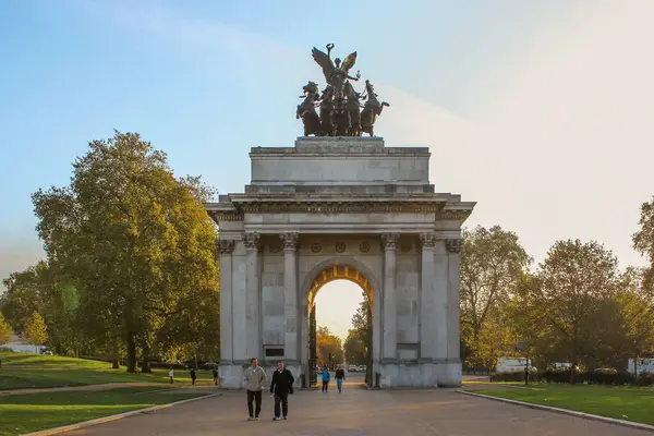 Londra 'daki ikonik Wellington Kemeri, sonbahar güneşinde ağaçlar tarafından çerçevelenmiş, aşağıda yürüyen ziyaretçilerle birlikte dimdik ayakta duruyor..