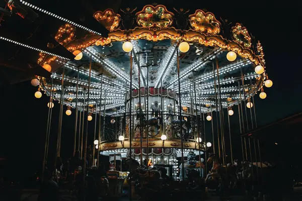 Gece parlak bir atlıkarınca, parlayan ışıklar renkli figürleri aydınlatıyor ve lunaparkta büyülü bir atmosfer yaratıyor..
