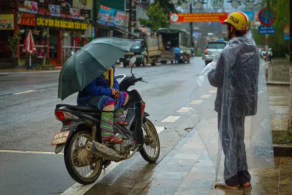 Şemsiyeli bir motosikletli, yağmurlu bir günde yağmurlu bir sokakta duran yağmurlu pançolu bir motosikletli..