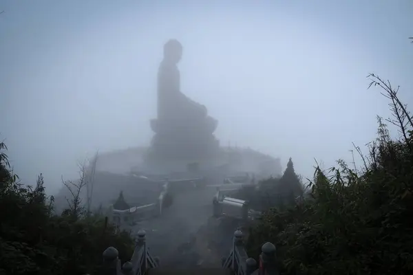 Bir dağın tepesine tünemiş, dumanla kaplanmış büyük bir Buda heykeli, üzerine çıkan taş adımlarla, dingin ve mistik bir atmosfer yaratıyor..