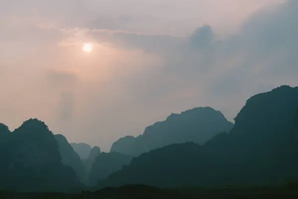 Ninh Binh, Vietnam 'ın karst dağları üzerinde puslu bir gün doğumu yumuşak bulutlar arasında huzur dolu bir parıltı bırakıyor ve sakin, atmosferik bir manzara yaratıyor..