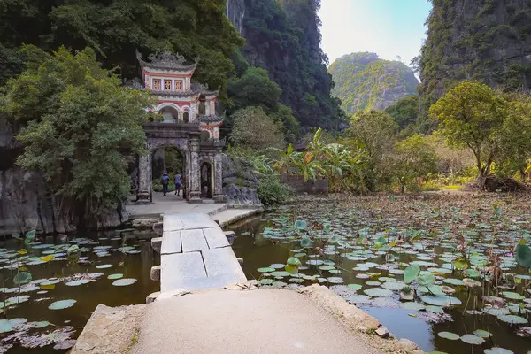 Bich Dong Pagoda 'daki geleneksel bir Vietnam kapısının huzurlu manzarası. Nilüfer havuzunun üzerinden geçen taştan bir patika, yemyeşil uçurumlarla çevrili..