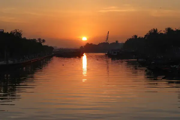 Hoi An, Vietnam 'da gün batımında güneş, suyun, ağaçların ve teknelerin gölgelerinin üzerine sıcacık yansıyor..