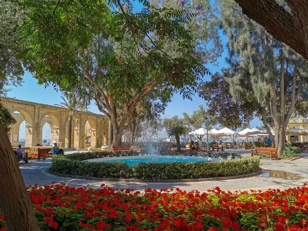 Valletta, Malta 'daki Yukarı Barrakka Bahçeleri' nde çeşmesi, kemeri ve kırmızı çiçekleri olan güzel bir bahçe..