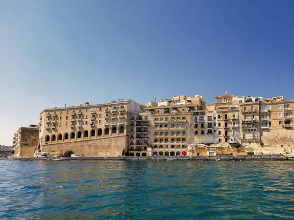 Valletta, Malta 'daki tarihi rıhtım binaları, parlak bir gökyüzünün altındaki açık mavi denize bakıyor..
