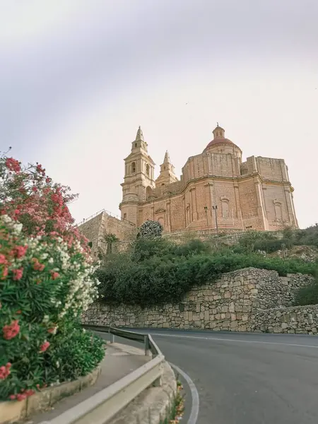 Malta 'da açık bir gökyüzüne karşı kurulmuş, çiçek açan ve taş duvarları olan görkemli bir tepedeki kilise..