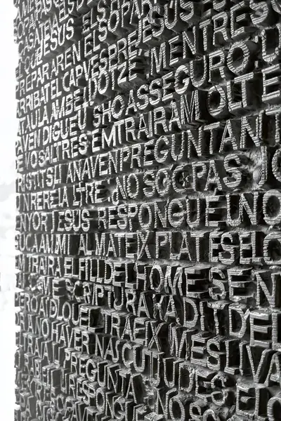 Close-up of a textured wall featuring raised letters arranged in a script, with a focus on intricate typography and details.