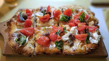 Çeri domatesli taze pişmiş pizza, mozarella, zeytin, ançüez ve ahşap bir tahtada fesleğen..