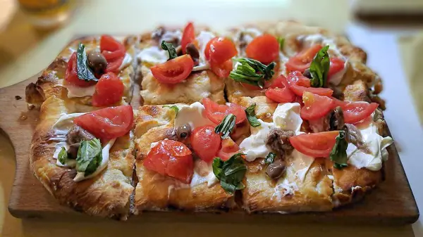 Çeri domatesli taze pişmiş pizza, mozarella, zeytin, ançüez ve ahşap bir tahtada fesleğen..