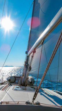 Güneşli bir günde yelken açarak yelken açmak. Güverteden manzara, parlak deniz, parlak güneş ve berrak mavi gökyüzü, denizde özgürlük ve macera yakalıyor.