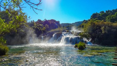 Hırvatistan 'ın Krka Ulusal Parkı' ndaki Skradinski buk şelalesi, güneşli bir günde yeşil ağaçlar ve temiz suyla çevrili..