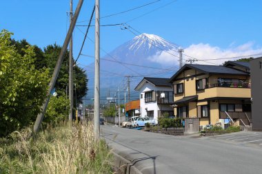 Karla kaplı Fuji Dağı açık mavi gökyüzünün altında, Japonya 'da sakin bir yerleşim yerinin arka planında yükseliyor..