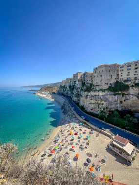 Tropea, İtalya 'da renkli şemsiyeler, turkuaz deniz ve sarp kayalıkların tepesindeki binalarla dolu bir sahil manzarası..