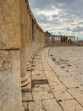 Ürdün 'ün Jerash kentindeki Oval Forum' un kıvrımlı sütununda taş kaldırım ve arka planda dramatik bulutlu bir gökyüzü var..