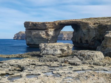 Gökyüzü bulutlu, mavi denizi ve kayalık kıyı şeridi olan, Malta 'daki Gozo Adası' nda doğal bir kireçtaşı kemeri..