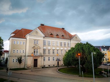 Kırmızı kiremit çatılı ve simetrik pencereli tarihi okul binası, Çek Cumhuriyeti 'nde sokak lambaları açık ve bulutlu bir akşamda çekildi.