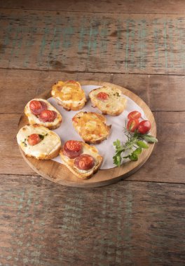 Erimiş peynirli ekmek dilimlerinde pişirilmiş bruschetta koleksiyonu, ahşap masa üzerinde kadife kuyruklu kiraz domatesleri açı manzaralı.