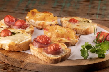 Eritilmiş peynirli ekmek dilimlerinde pişirilmiş bruschetta koleksiyonu, ahşap masa üzerinde kiraz domatesleri ön cepheden yakın çekim açısında.