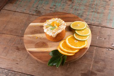 Portakal dilimli turuncu pasta ve üzerine beyaz krema. Kırsal ahşap masa ve portakal dilimleri.