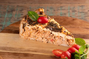 Bir dilim baharatlı tavuk turtası kekik hamurlu ve kiraz domatesli yuvarlak ahşap bir tahta üzerinde, kırsal bir masada, dolgunun kenarına yakın plan