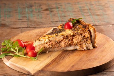 Bir dilim baharatlı tavuk turtası kekik makarnalı ve kiraz domatesli yuvarlak ahşap bir tahta üzerinde yakın plan masa.