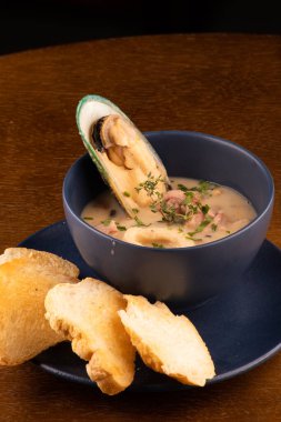 Bir kase kızarmış Yeni Zelanda midyesi ve ahşap masa köşesinde yeşil soğanlı deniz ürünleri çorbası.
