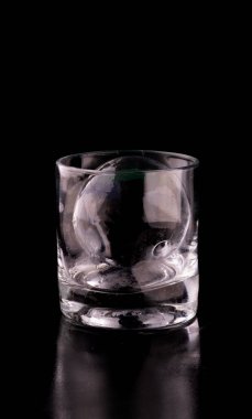 Konyak içinde kristal saydam buz ve küre ve siyah zemin üzerinde viski bardağı yansıması.