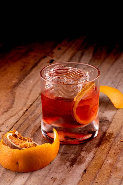 素朴な木のテーブルにオレンジ色の皮で装飾されたオレンジと半透明なアイスとネグロニカクテルドリンクのファイングラス — ストック写真