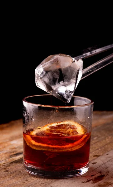 黒い背景にオレンジ色のクローズアップと木のテーブルにカンパリとマウスと赤いネグロニの飲み物にダイヤモンドの氷を入れる — ストック写真