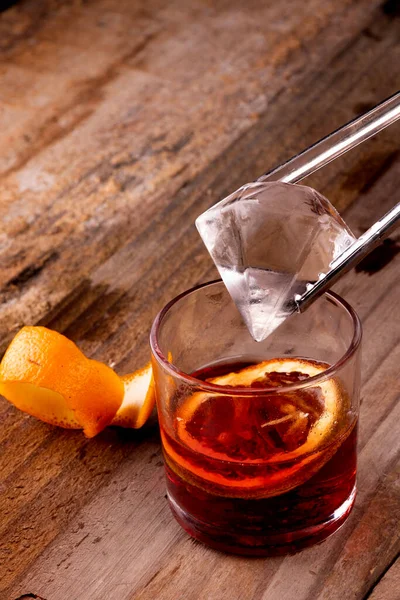 ダイヤモンドの氷をカンパリとオレンジ色の木のテーブルの上に赤いネグロニの飲み物に置く — ストック写真