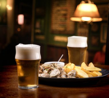 Barda bir buçuk litre bira ve patates kızartması ve sosis arkaplanda bulanık bir porsiyon yemek.