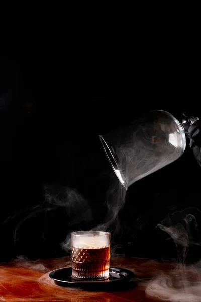 removing the drink smoker from a glass of smoked whiskey with smoke on a wooden table