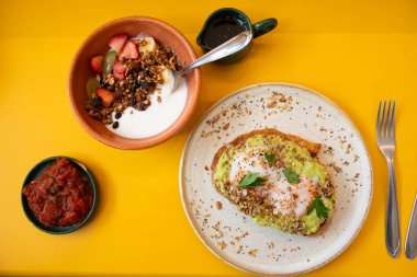 domates tostlu sağlıklı protein kahvaltı tabağı avokado ve yumuşak yumurta sarısı ve meyveli yoğurt ve tahıl gevreği.
