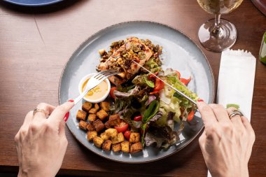 Hafif ızgara somon salatalı tost ve beyaz şaraplı kadın eli.