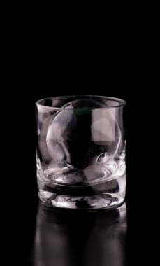 Konyak içinde kristal saydam buz ve küre ve siyah zemin üzerinde viski bardağı yansıması.