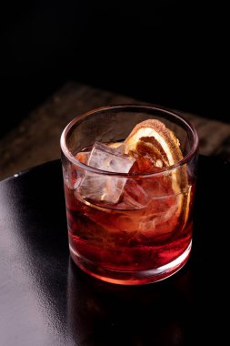 Kırmızı negroni içeceği, campari ve vermut ile ahşap masanın üzerinde portakal rengi yakın plan bulanık arka plan.