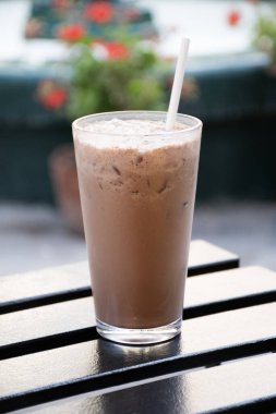 Tahta masada çikolatalı milkshake smoothie ve arka planda bulanık çiçek bahçesi.