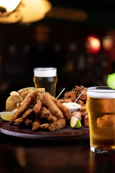 portion of seafood with breaded fish and shrimp and grilled salmon with fries and two glasses of craft beer blurred background in pub