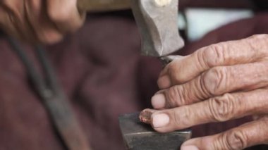 Yaşlı bir demirci, metal bir parçayı çekiçleyip rafine ederek dekoratif bir kolye yapıyor. Ladakh, Hindistan