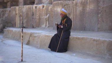 Bedevi bir adam piramit taşına oturur ve ağzına sigara koyar, Giza, Mısır