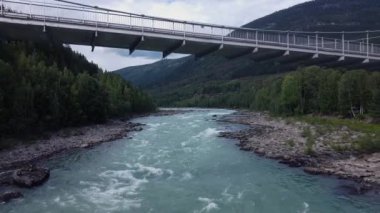 Norveç Sjoa Nehri köprüsü altındaki hava aracı manzarası dağlık ormanlarla çevrili.