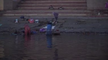Kadın ve erkek, şafakta Varanasi 'deki Ganj Nehri' nin kıyısında çamaşır yıkıyor..
