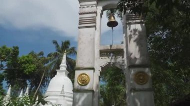 Beyaz çan kulesi. Etrafı yeşillik ve beyazlarla çevrili.