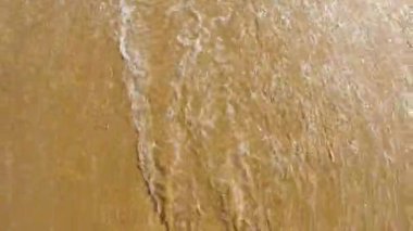 Okyanus dalgalarının üst görüntüsü sürekli olarak altın kumlu bir plajın üzerinde süzülüyor..
