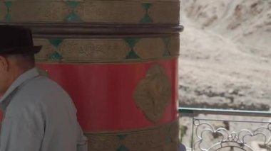 Şapkalı yaşlı adam Ladakh 'ta Budist dua çarkını döndürüyor.