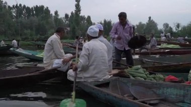 Bir adam şafaktan önce Srinagar 'da yüzen markette yeşillikleri tartıya koyar.
