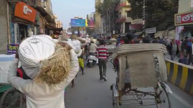 Seyyah bir adam Varanasi 'de kalabalık bir caddede saman çuvalı taşıyor.
