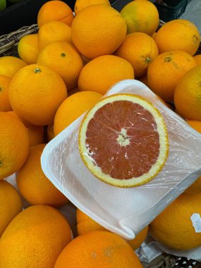 Dilimlenmiş bir greyfurt ile canlı bir portakal gösterisi. Plastiğe sarılı, hasır sepete yaslanmış, taze ve sulu..