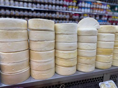 Yuvarlak, kremsi peynir dilimleri süpermarketin içindeki bir rafta dizilir ve arka planda renkli baharatlar görünür..