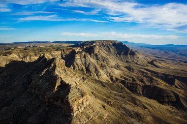 Berrak mavi gökyüzünün altındaki uçsuz bucaksız dağlık bir arazinin nefes kesici hava manzarası. Engebeli arazide dramatik tepeler ve gölgeler yer alıyor, doğanın saf güzelliğini gözler önüne seriyor & 39; 'un oluşumları.